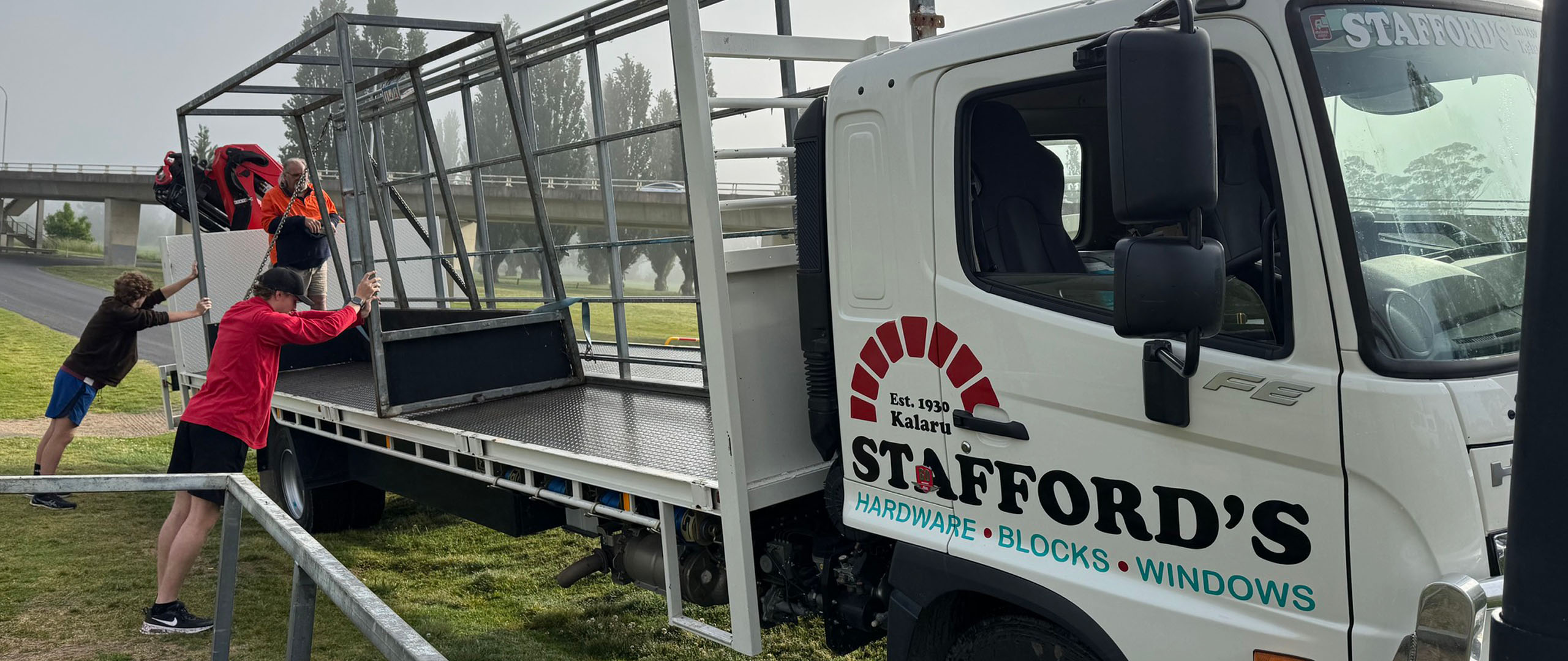 Stafford’s Hardware truck delivering goalposts for Tathra United Football Club, with volunteers unloading them from the back. The Stafford’s branding is visible on the truck’s cabin door.