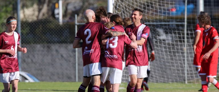 A group of Tathra United football players gather on the field, smiling and patting each other on the back after a successful play.