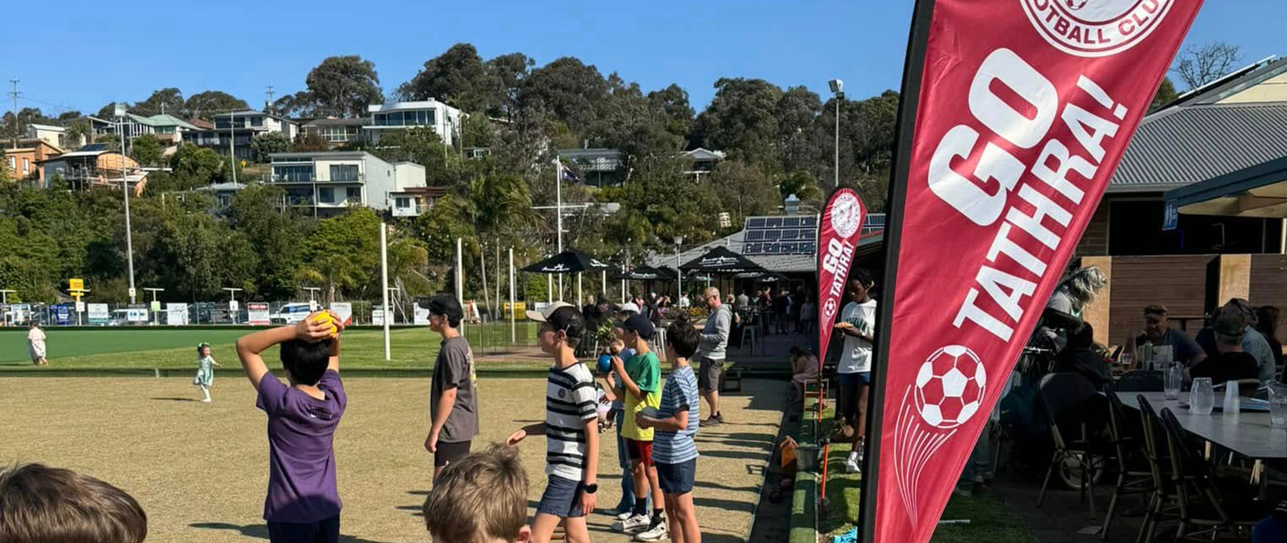 A snapshot of the Tathra United Football Club game day, featuring team flags waving and spectators gathered along the sidelines.