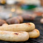 Close-up of sausages sizzling on a barbecue, with grill marks forming as they cook over the heat.