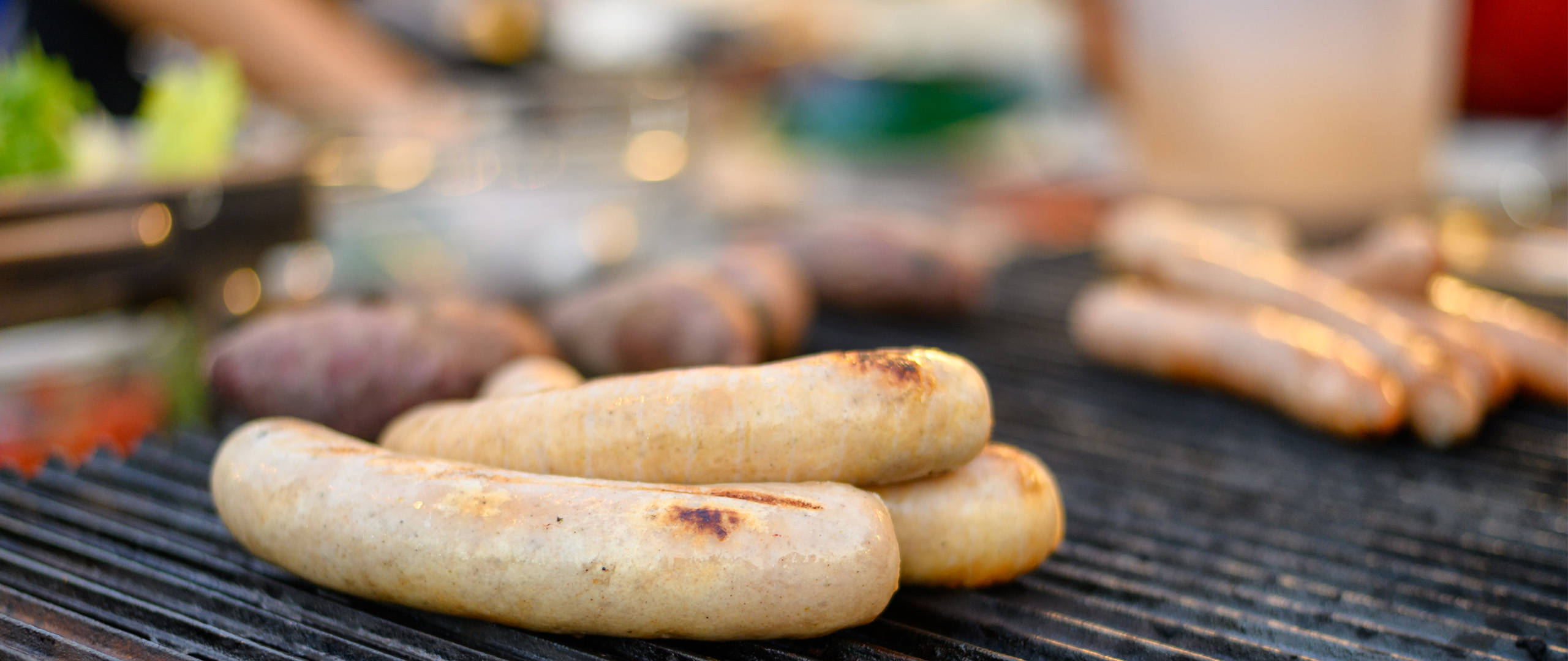 Close-up of sausages sizzling on a barbecue, with grill marks forming as they cook over the heat.